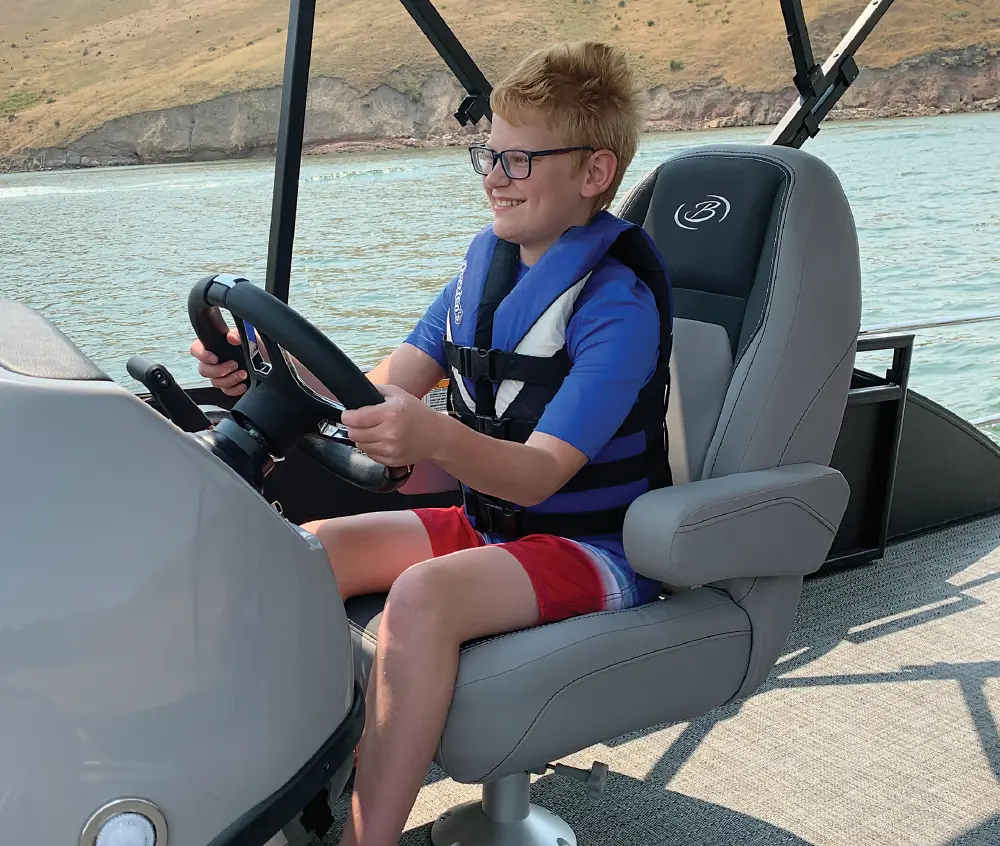 A young person steering a boat on a sunny day with hills in the background.