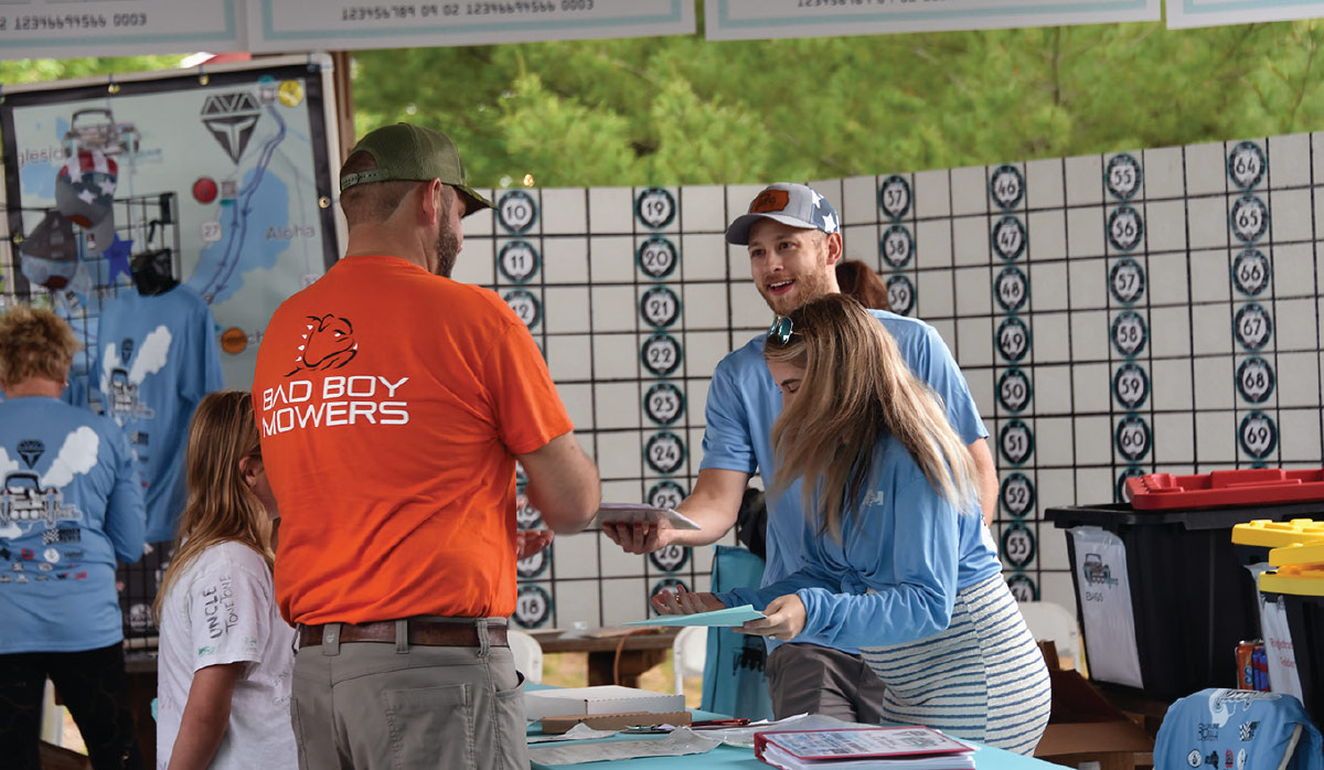 man at booth talking to another man and woman behind the table