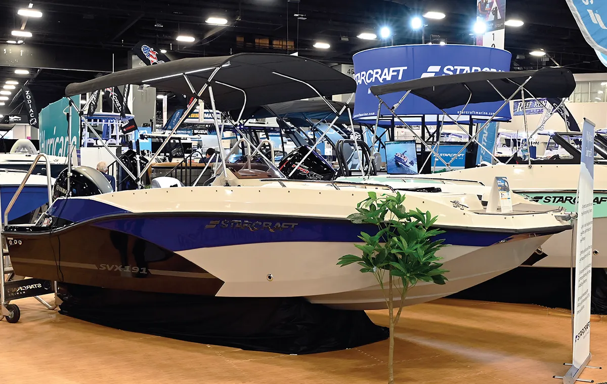 A Starcraft SVX 191 boat displayed indoors with a black canopy and white exterior featuring navy accents.