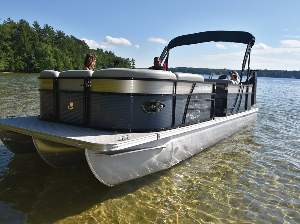 A pontoon boat on a lake with people on board, surrounded by trees.