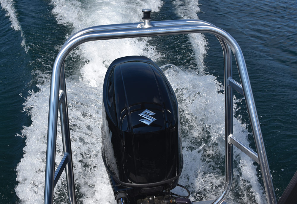 Back view of a boat's black outboard engine creating a foamy wake.