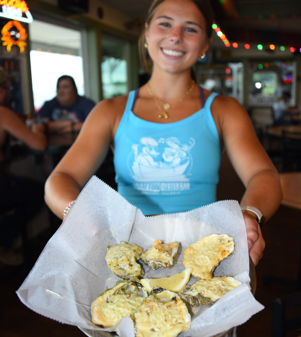 Smiling woman presenting a plate of baked oysters topped with cheese.