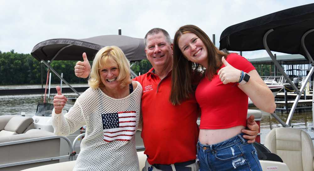 Three people smiling and giving thumbs up on a boat dock.