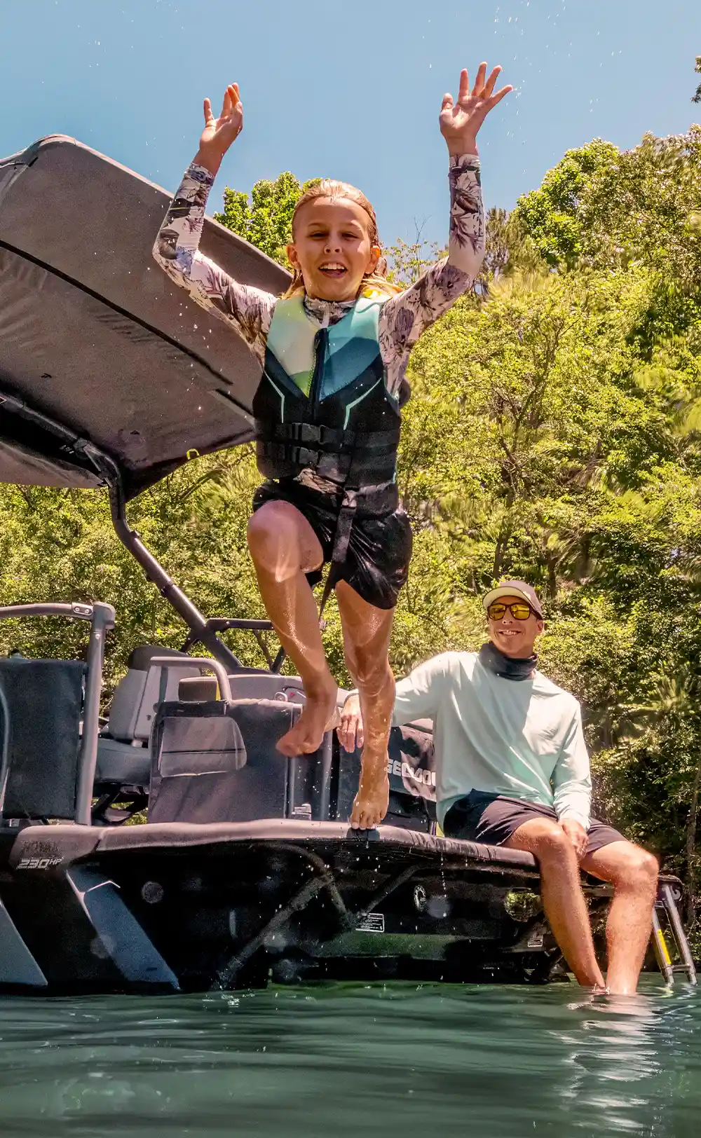 girl excitedly jumping off the edge of a pontoon while a man watches with a smile