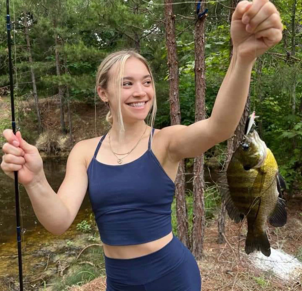 girl smiling while holding a sunfish attached to fishing lure