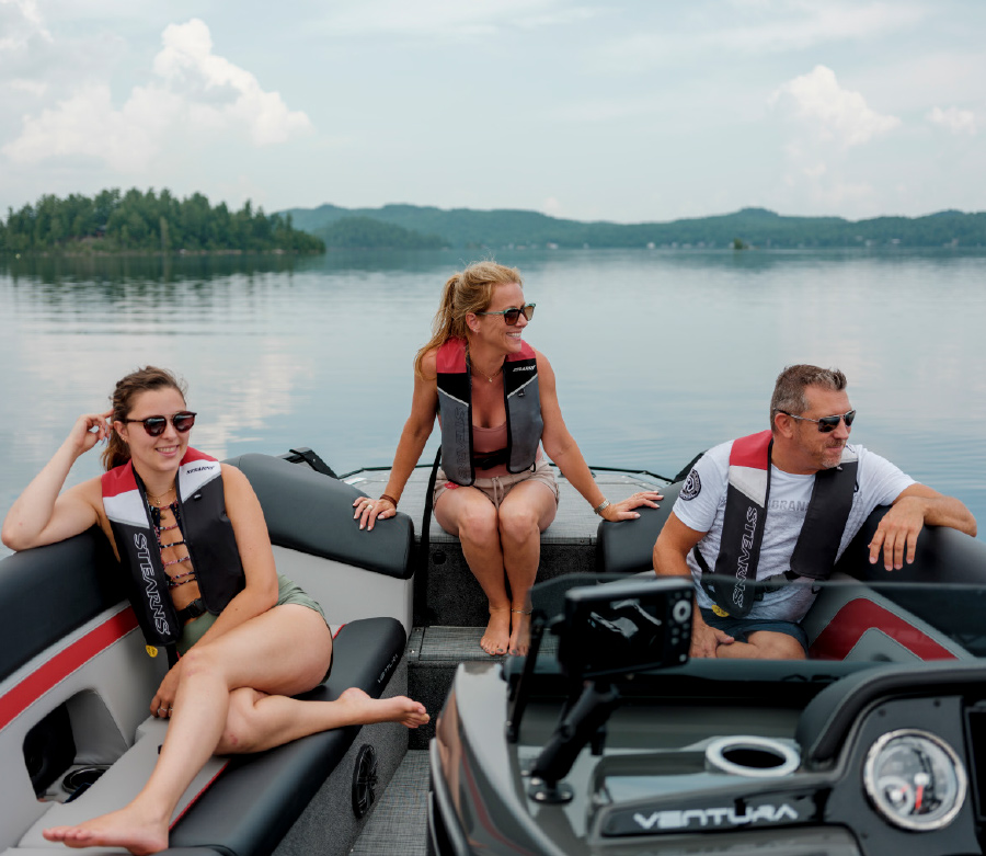 a man and two women sitting near rear of pontoon with mountainous landscape behind them