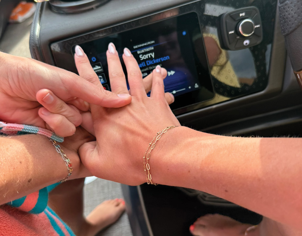Close-up of two hands near a radio screen displaying a song title.