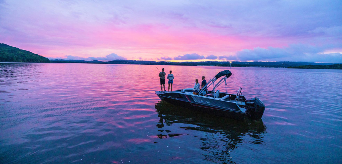 People on a boat on a lake at sunset with a pink and purple sky.