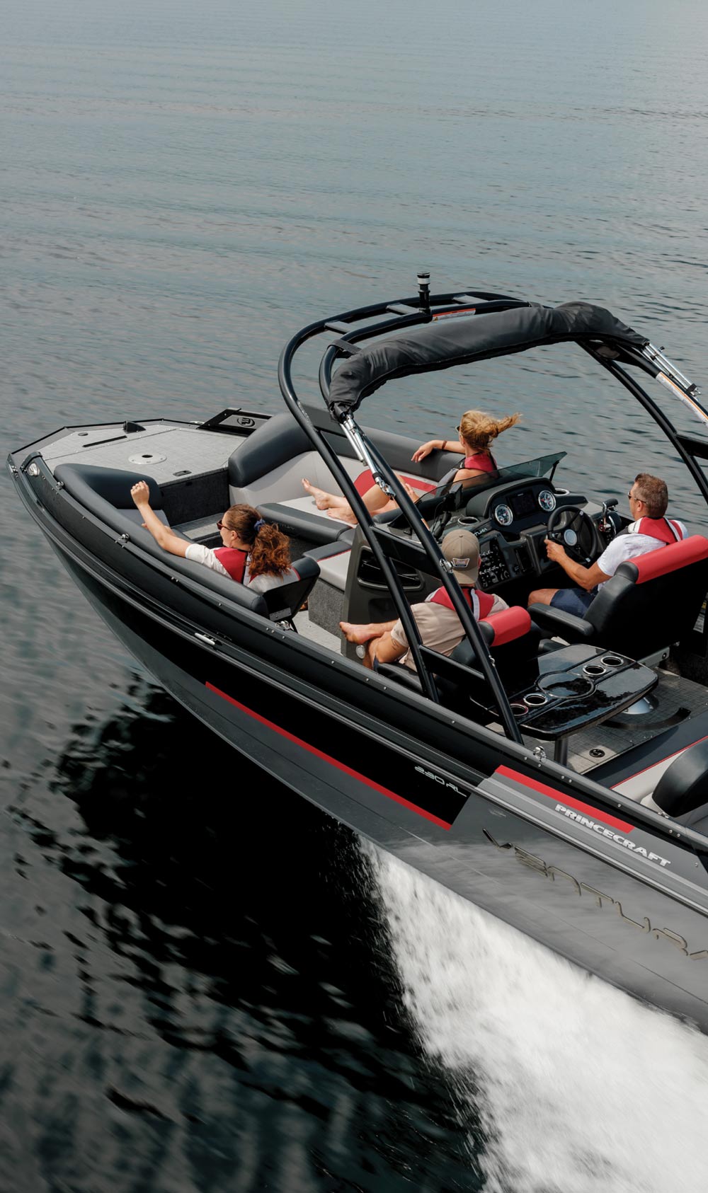 A modern motorboat with four people, moving through calm water.