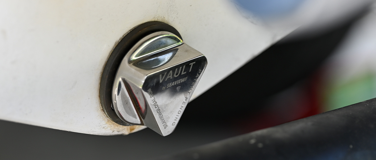 Close-up of a 'Vault by Seaview' boat drain plug made of polished metal, installed on the hull of a white boat.