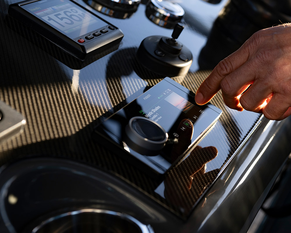 close up of a hand tuning the Fusion Apollo RA800 marine stereo on the helm dashboard of a pontoon