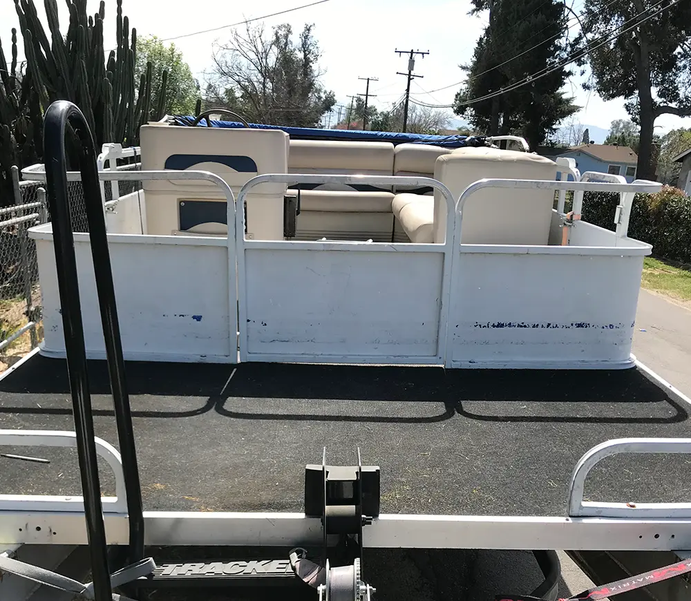 A worn-out pontoon boat with faded white railings and dirty vinyl seating, seen from the rear.