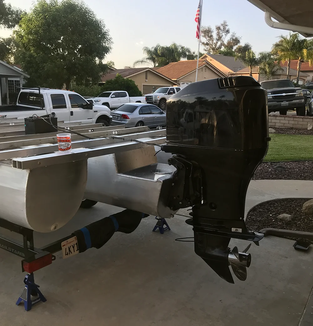A newly installed black outboard motor on the back of a pontoon boat frame and trailer in a driveway at sunset.