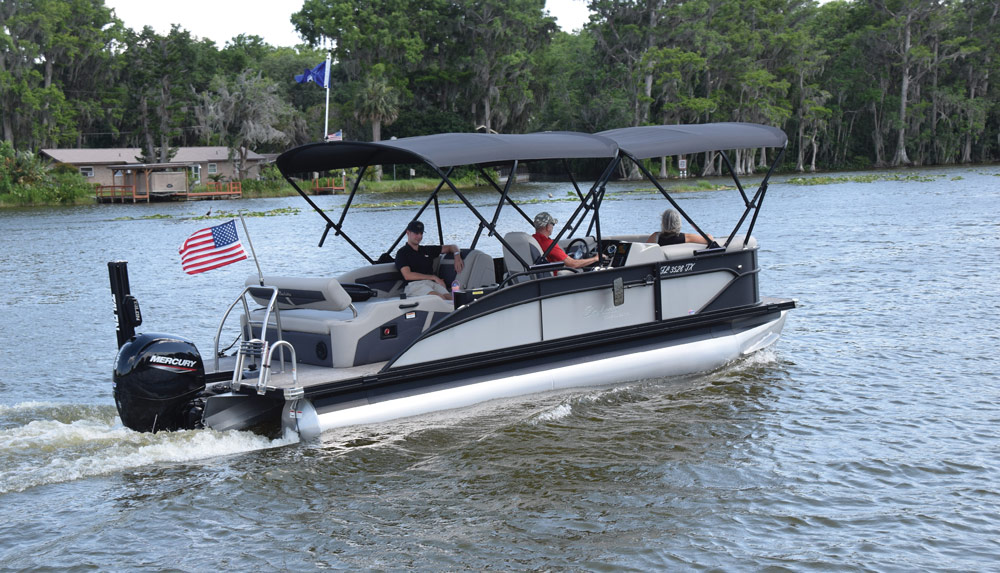 Pontoon boat with a Mercury motor on a body of water, featuring three canopies and an American flag.