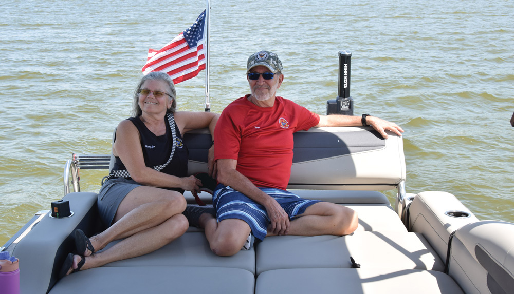 Two people relaxing on a boat with an American flag and water in the background.