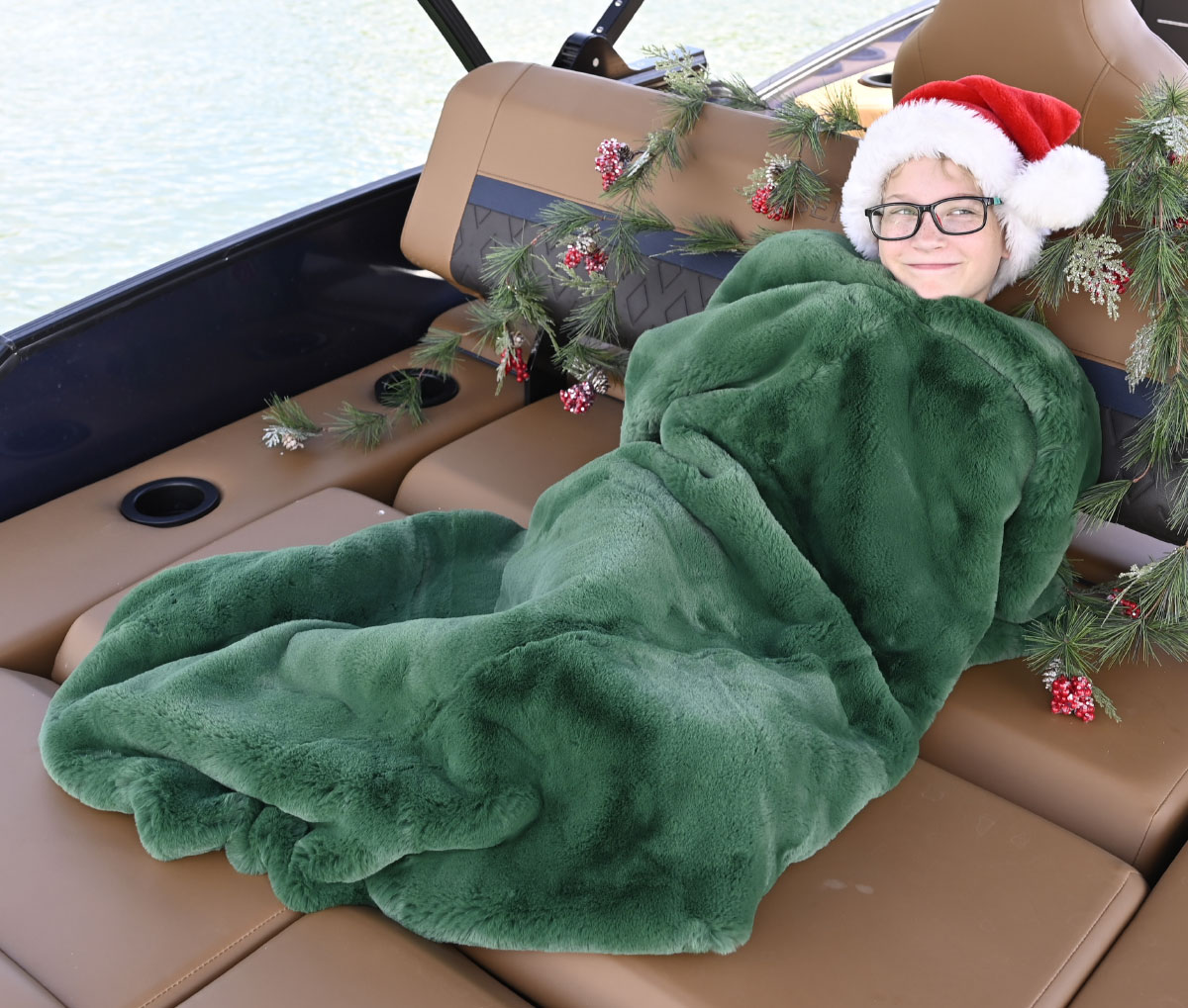 young boy on pontoon wrapped in Pretty Rugged Blanket while wearing a santa hat