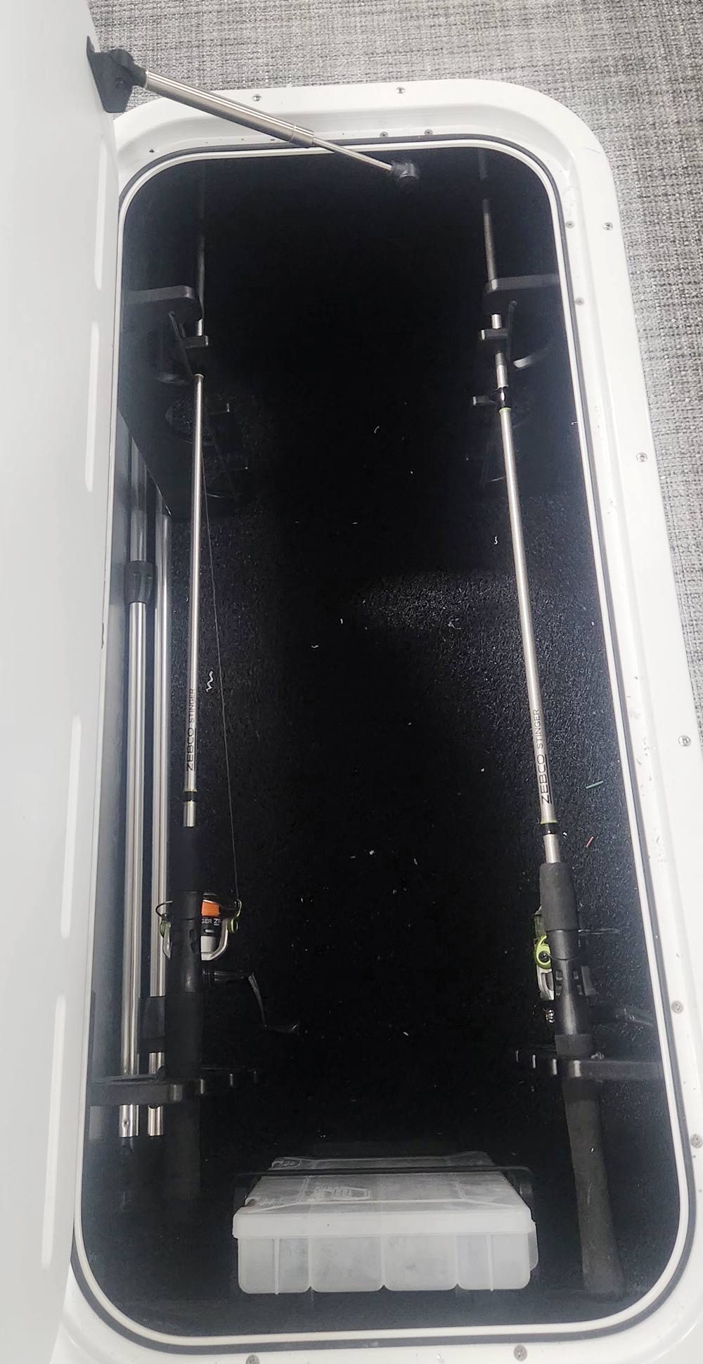 An open boat storage compartment showing two fishing rods and reels secured vertically to the side walls.