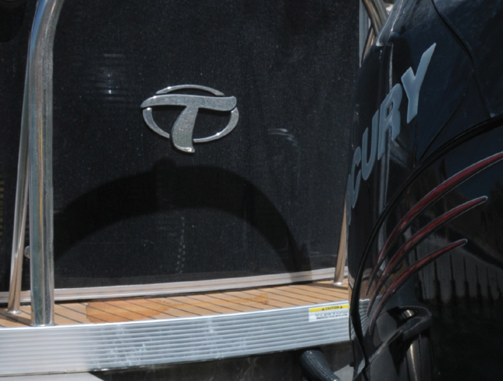 A close-up of a pontoon boat's stern, showing a Mercury outboard engine and the boat's "T" logo.