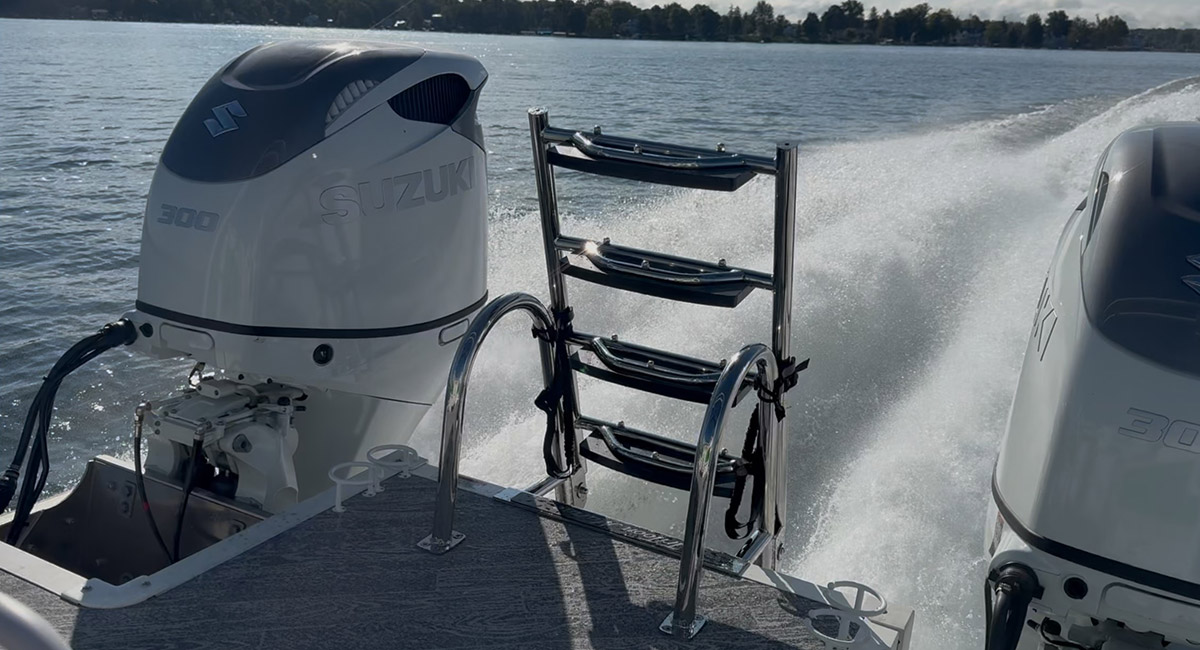 cropped view of the laddered stern of a JC TriToon pontoon with two white Suzuki outboards