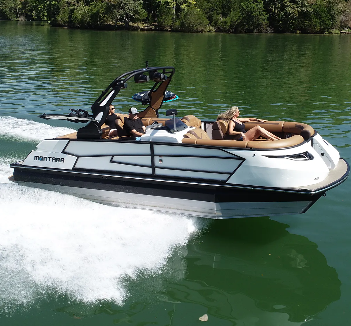 starboard side view of a white Montara Boats pontoon sailing on a body of water lined by trees in the background