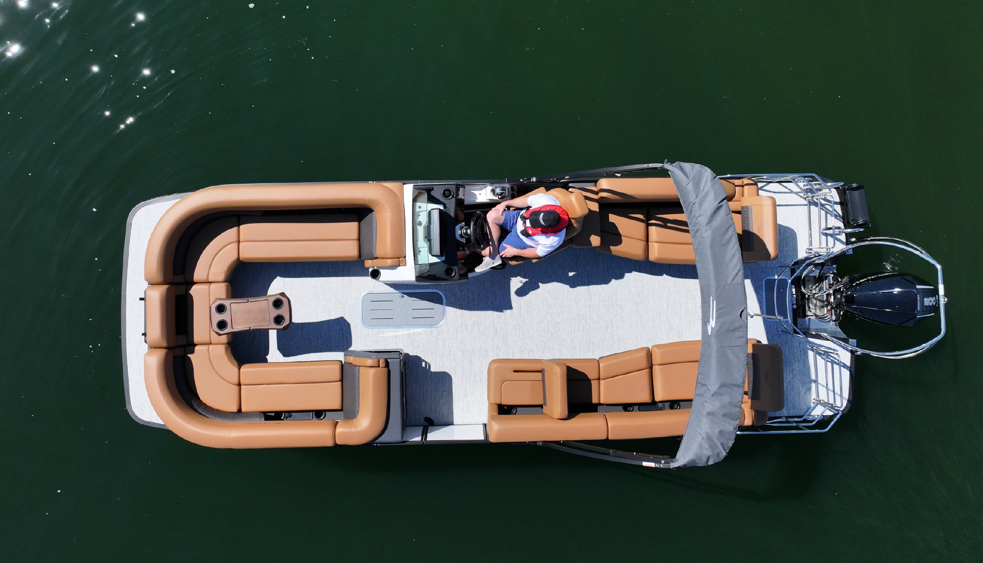 Aerial high top view of a man seated in a driver's seat of a Bennington 24MSL motorboat vehicle as it is stationary idle in a body of water
