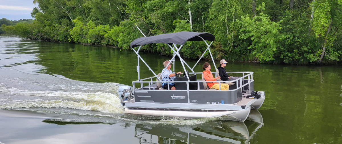 Three people inside a NorthStar pontoon motorboat vehicle as it is being driven out on the water