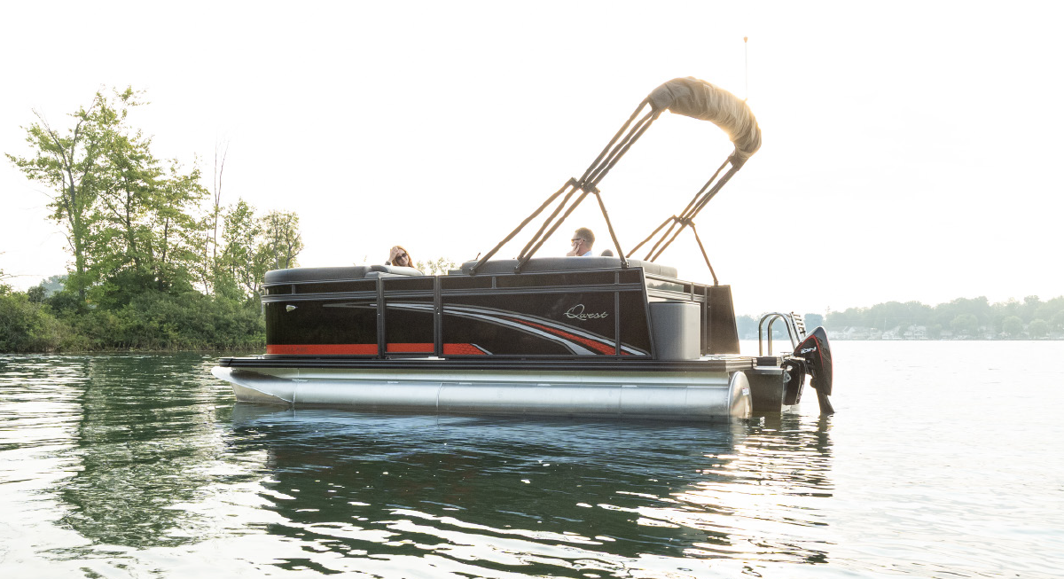 Two people inside a Qwest C-Class Cruise pontoon motorboat vehicle as it is stationary out on the water