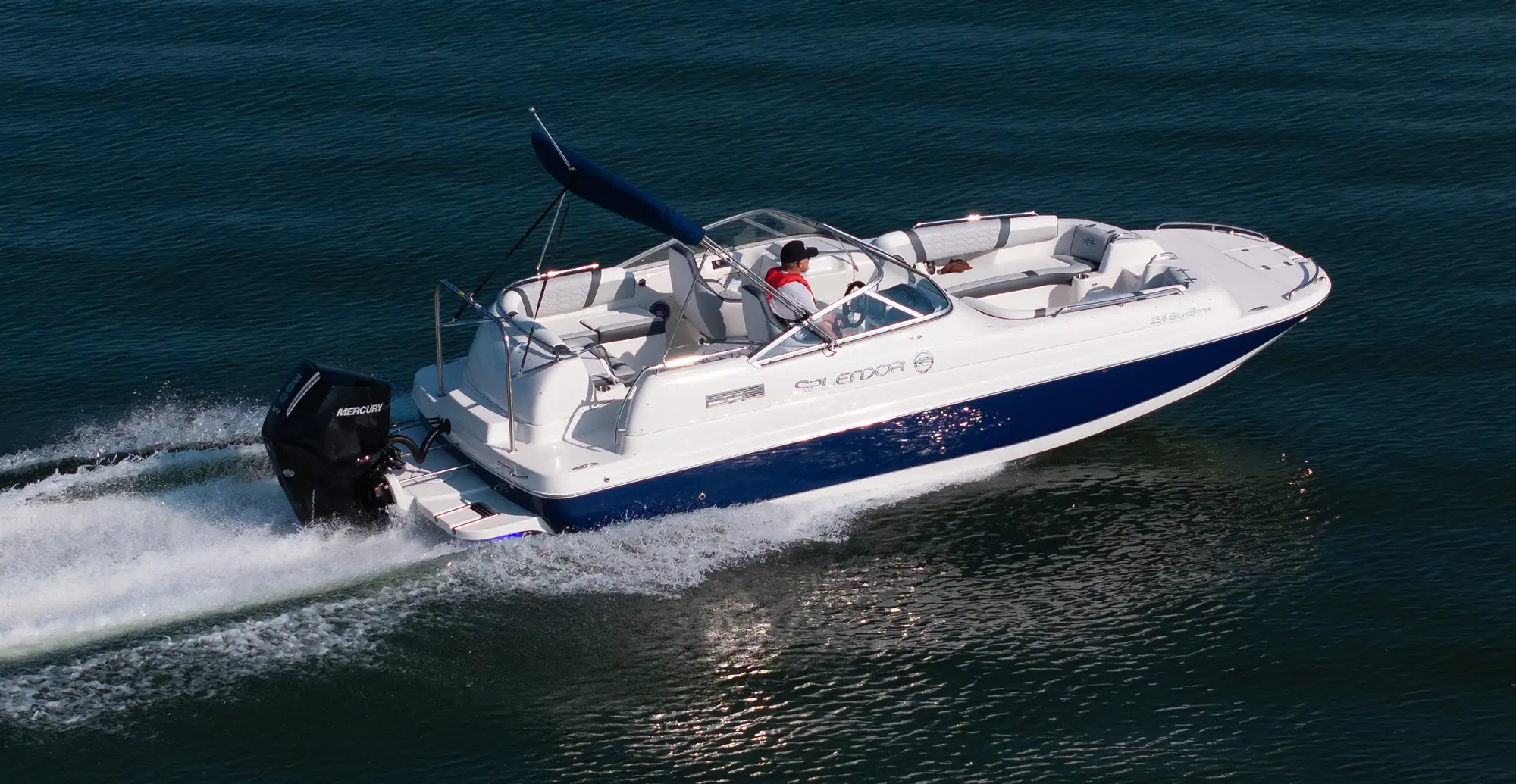 A white and blue Splendor 259 SunStar deck boat cruising on open water with a black Mercury outboard motor.