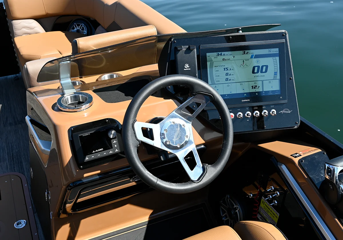 Close-up of a luxury pontoon boat's driver station showing integrated JL Audio controls, a digital engine monitor, and premium tan upholstery.
