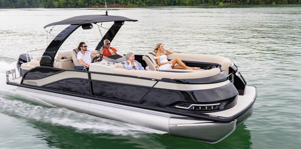 A tan and black Harris pontoon boat carries four passengers. It features a unique curved black tower with a sunshade and luxurious, deep-cushioned lounge seating in the bow.