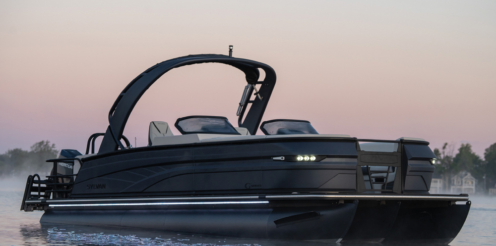 A matte black Sylvan G-Series pontoon boat at dawn. The image showcases integrated LED docking lights and a prominent, architectural black sport tower.