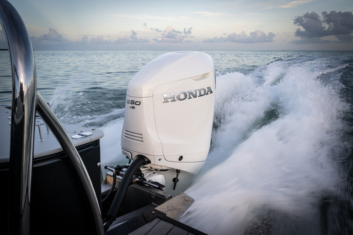 Close-up of a white Honda 350 V8 outboard motor powering a boat through choppy blue water, creating a large white spray of wake against a sunset horizon.