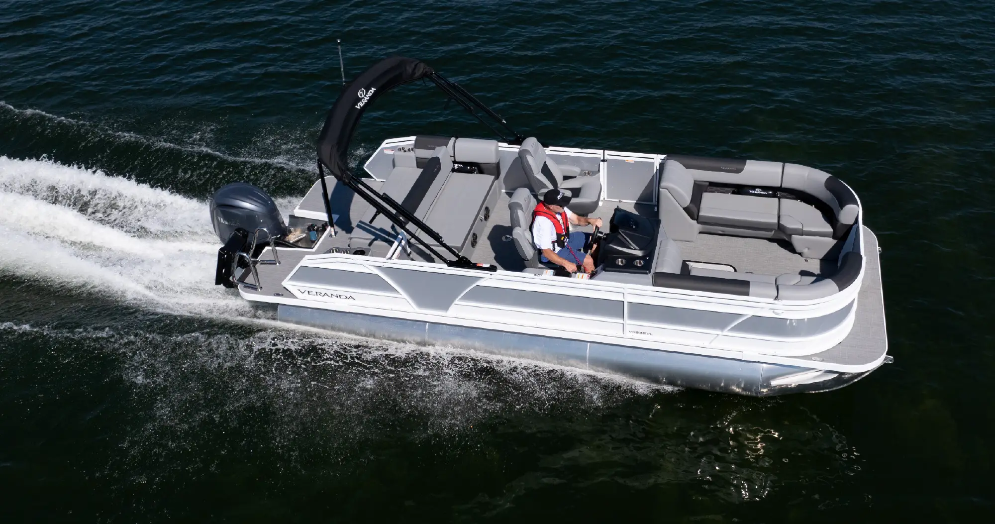 A light grey Veranda pontoon boat with dark accents cruising quickly on dark blue water, leaving a white wake.