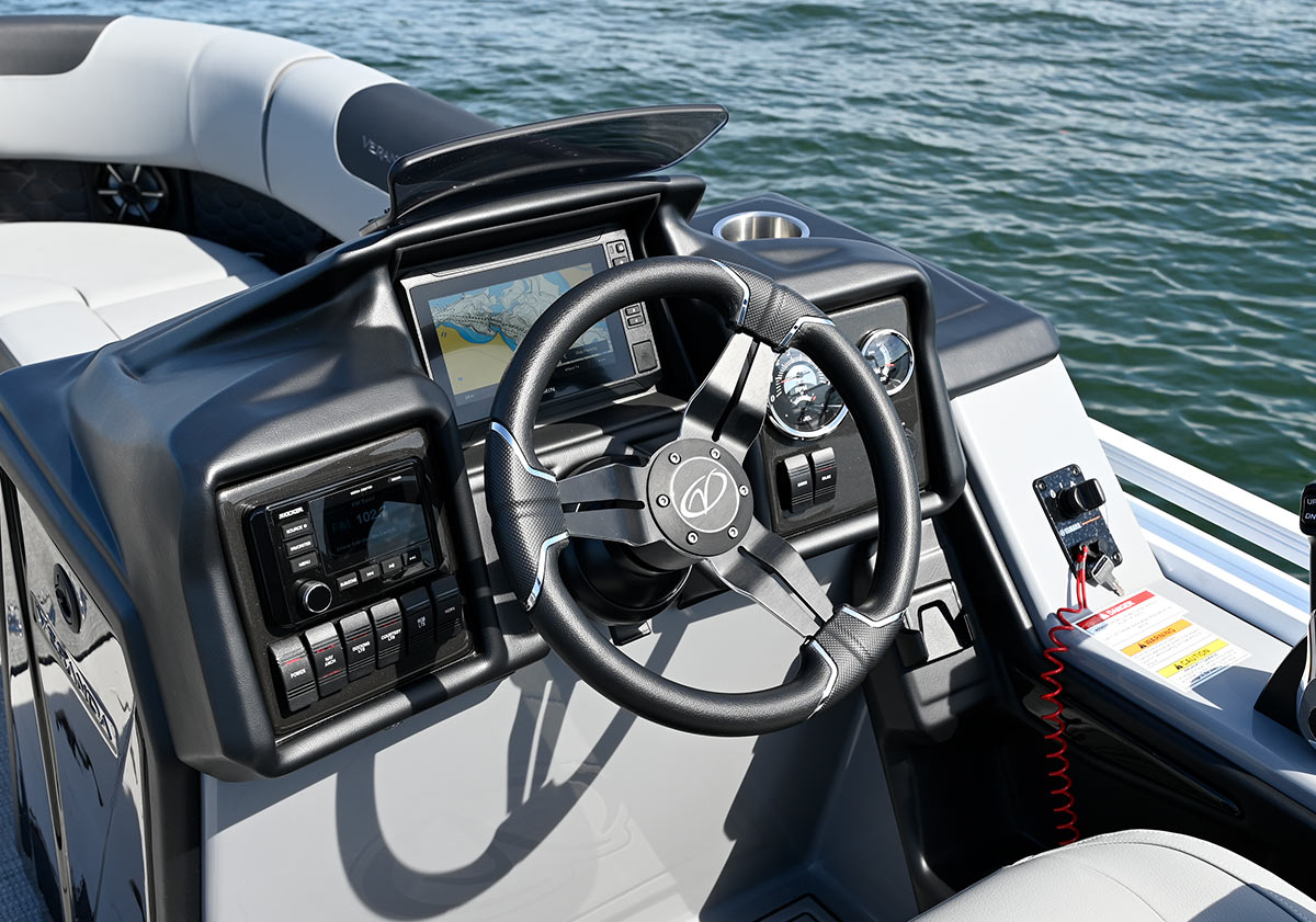Detailed shot of a grey boat console with a Garmin touchscreen, a black steering wheel, a Kicker stereo, and a red kill-cord.