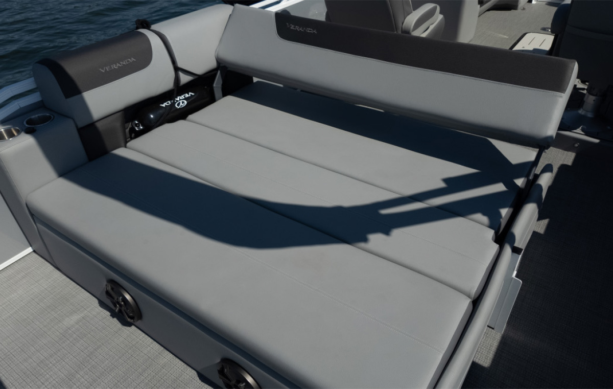 View of a grey cushioned sun pad on a boat deck with the Veranda logo on the backrest and a black accessory bag tucked in the corner.