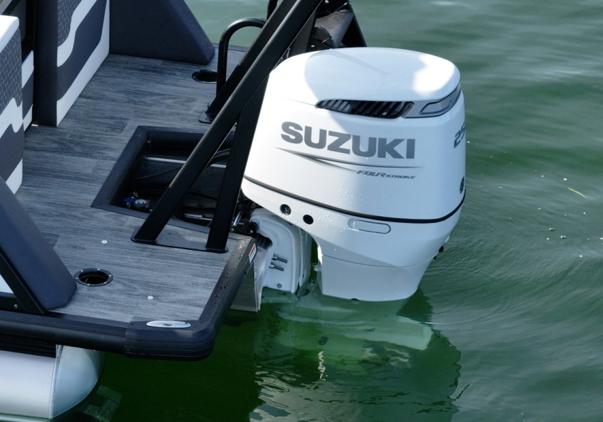 Close-up of a white Suzuki outboard motor mounted on the grey wood-plank deck of a boat in green water.