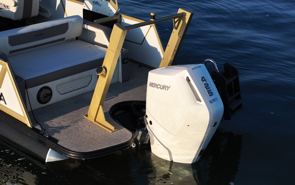 Close-up of the boat's stern featuring a white Mercury 425 V10 outboard motor. A gold-painted tow pylon and a black boarding ladder are visible on the gray textured swim platform.