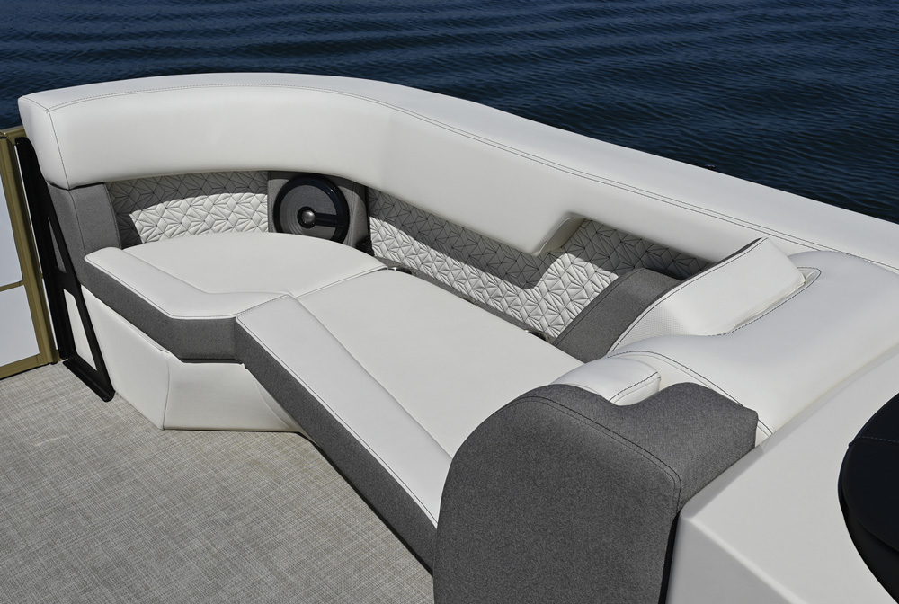 Close-up of the bow seating area showing premium white and gray upholstery with geometric patterned stitching. An integrated marine speaker is recessed into the side panel.