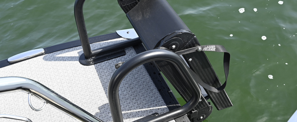 Close-up of a black folding boarding ladder on a boat deck with a gray textured surface, showing a black strap labeled "Ladder Release."