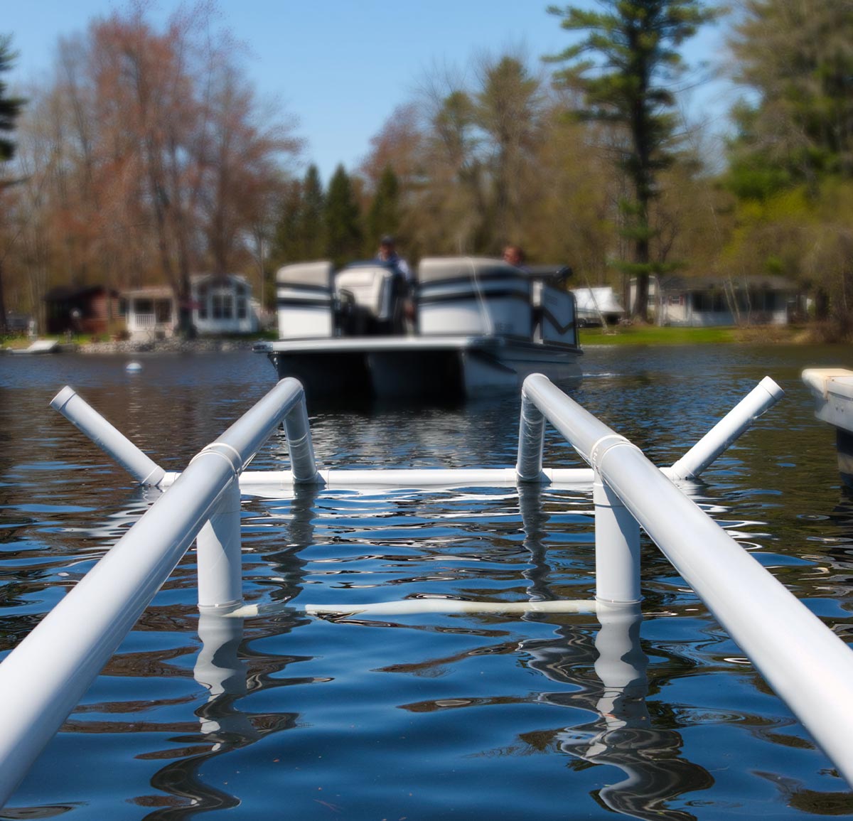 White parallel guide rails of the Docked entry system sit in calm water. A pontoon boat with two people on board approaches the bars from a distance.