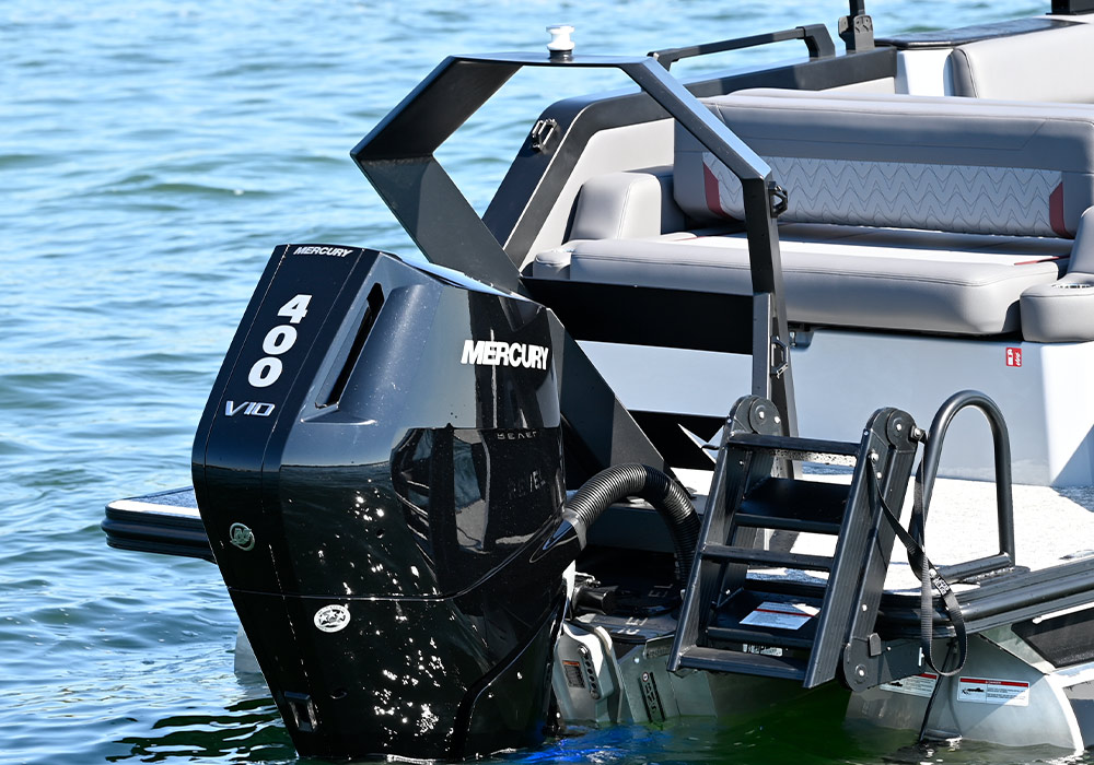 Rear view of the Revel RS25 stern featuring a black Mercury 400 V10 outboard motor. A black angular ski tow pylon stands above the engine, and a black four-step telescoping ladder is mounted to the starboard swim platform.