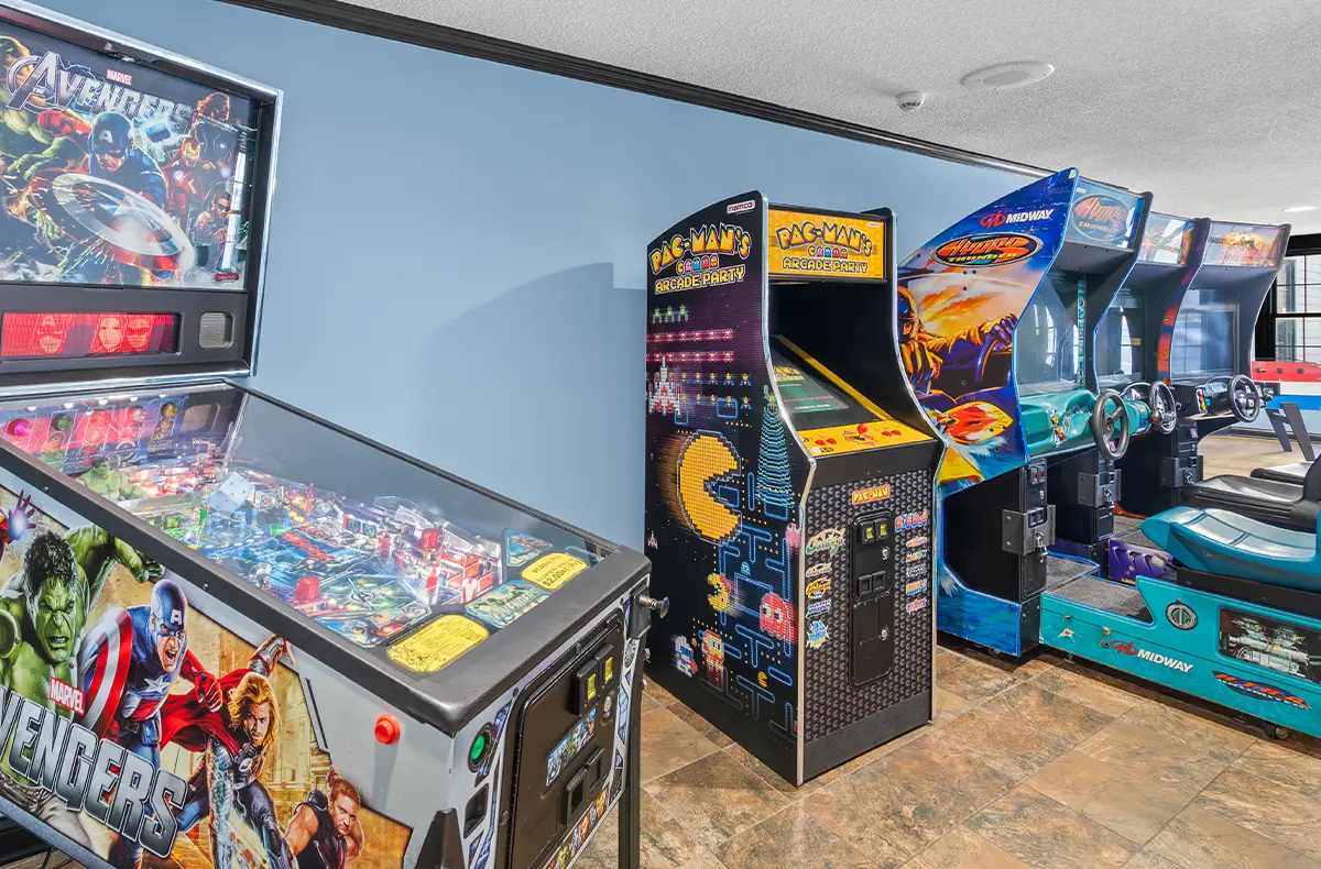 A bright and colorful game room at Oakwood Resort featuring an Avengers pinball machine, a Pac-Man's Pixel Bash arcade cabinet, and Hydro Thunder racing simulators.