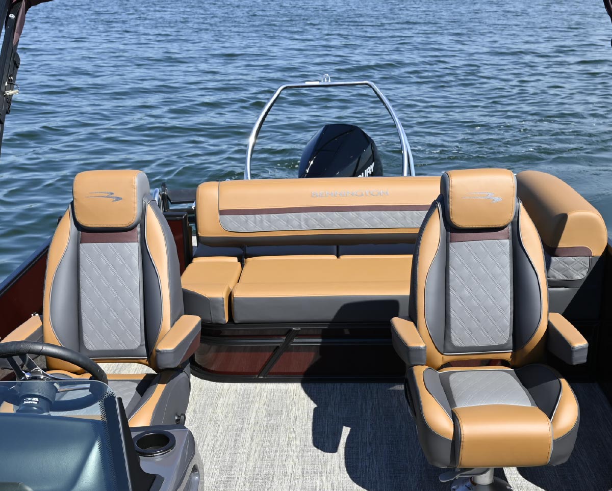 Interior view facing the rear of a pontoon boat, showing two captain's chairs and a large cushioned lounge area.