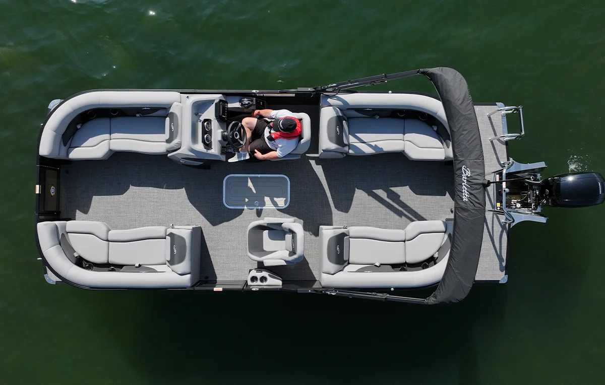 Top-down aerial view of a Barletta Aria pontoon boat on green water, showing the spacious floor plan with premium grey lounge seating and a captain’s station.