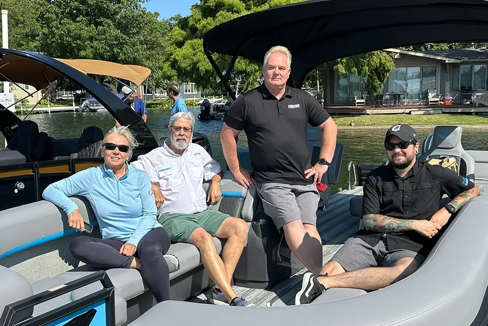 Four people are posing for a photo on a modern pontoon boat on a sunny day