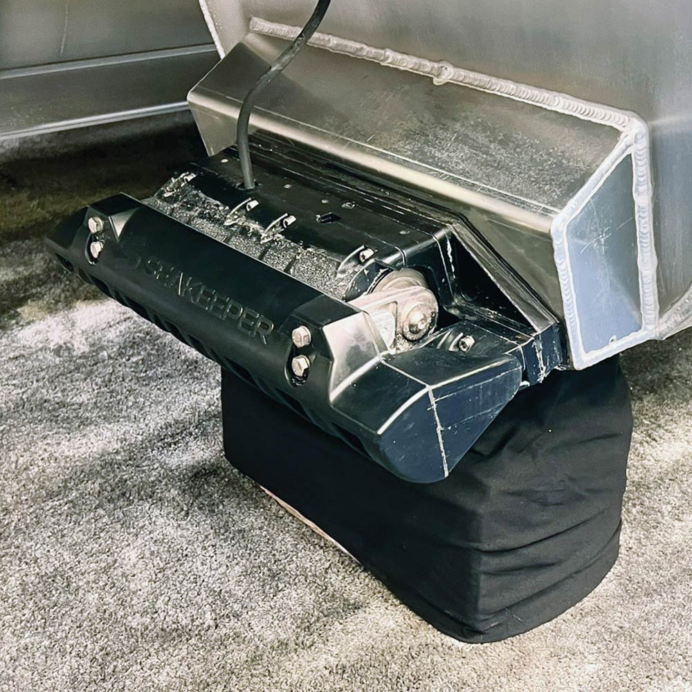 Close-up of a Seakeeper Ride system mounted to the transom of an aluminum boat hull. The black hardware is positioned above a black support block on a carpeted floor.