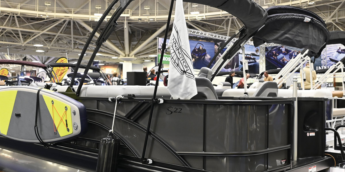 Side view of a Bennington S22 pontoon boat featuring a black railing, a white branded flag, and a grey and lime green paddleboard mounted to the exterior side of the hull.