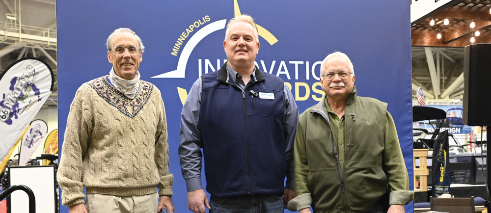 Three men pose for a photo in front of a blue "Minneapolis Innovation Awards" backdrop at a marine industry event, celebrating the year's top nautical advancements.