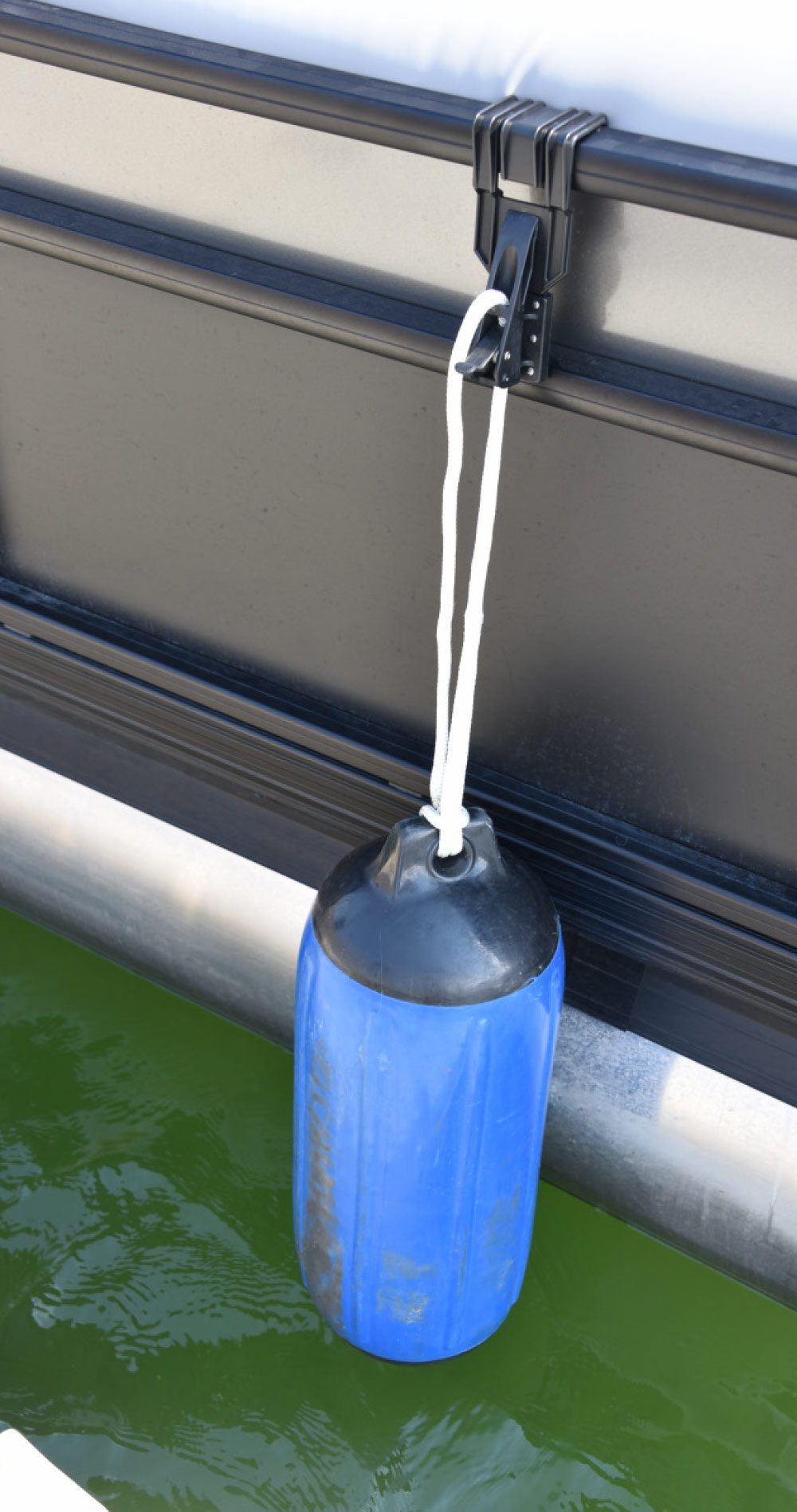 A blue and black boat fender hanging from a pontoon boat's side rail by a white rope to protect the hull while docking.