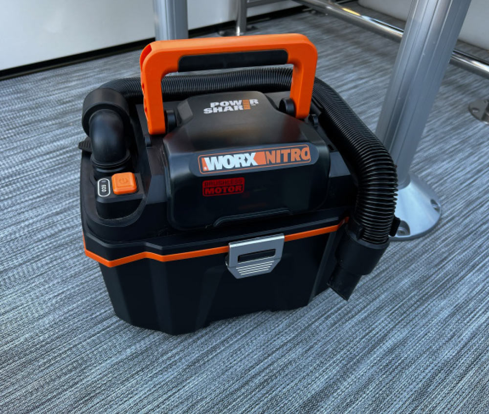 A black and orange Worx Nitro cordless wet/dry vacuum cleaner sitting on the grey textured floor of a boat.
